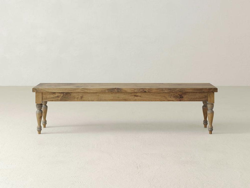 The Chateau Bench - Harvest Wheat by James & James stands against a plain white background, featuring four carved legs and a simple rectangular seat, showcasing its rustic design with a natural wooden finish.