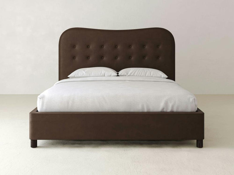 The James & James Florence Bed—Leather boasts a dark brown tufted headboard and light grey bedding, with clean lines and simple design that add a modern, minimalist touch against a plain white background.