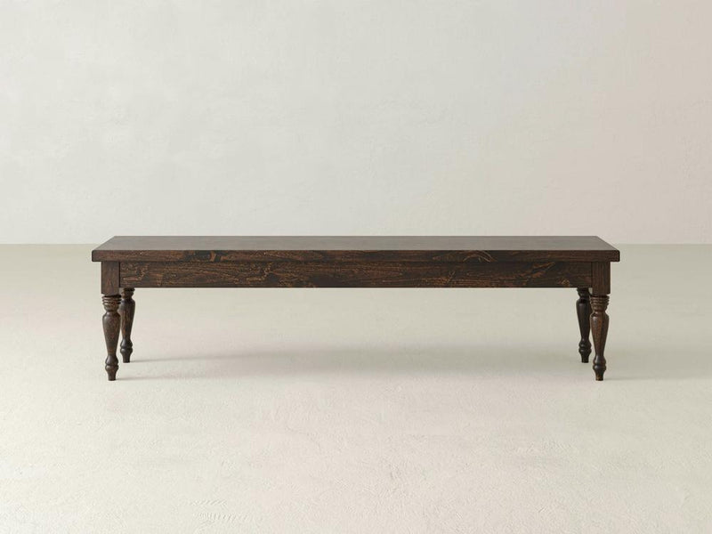 The James & James Chateau Bench - Tobacco features a simple, rustic design with dark wood and four turned legs, set against a plain, light-colored background.