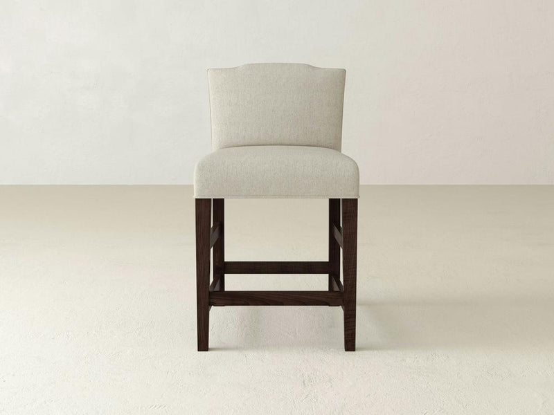 The Hadley Upholstered Stool by James & James features beige fabric, cushioned seat and backrest, sleek dark wooden legs, and a contemporary design that enhances any dining space against a light background.