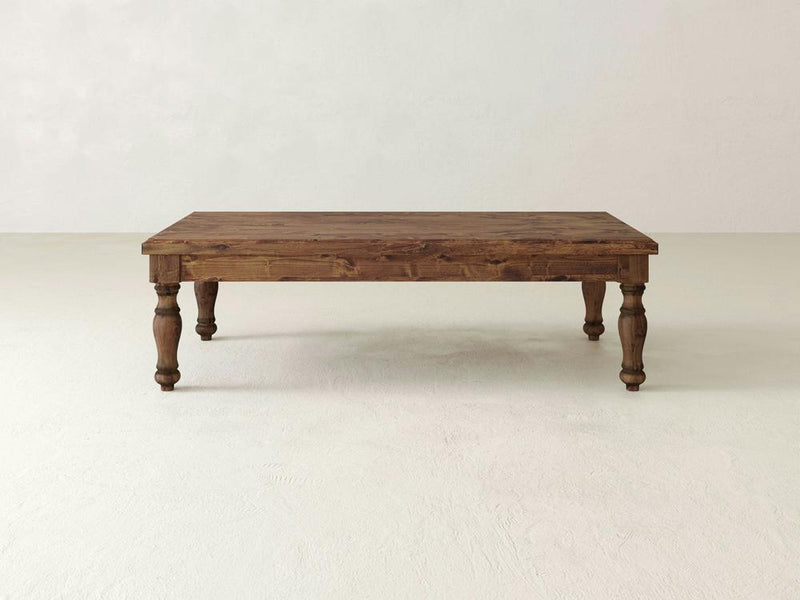 The Abigail Coffee Table - Tuscany by James+James features a rectangular wooden design with a dark brown finish, standing on four turned legs. Set against a plain, off-white background, the table's simple and rustic style beautifully showcases the natural wood grain and texture.