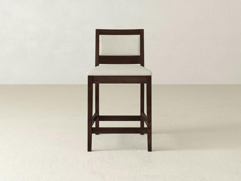 The Gina Side Stool by James & James showcases a sleek design with a dark brown maple frame and light beige cushioning. Perfect for minimalist, modern settings, it rests seamlessly on a plain beige floor against an off-white wall.