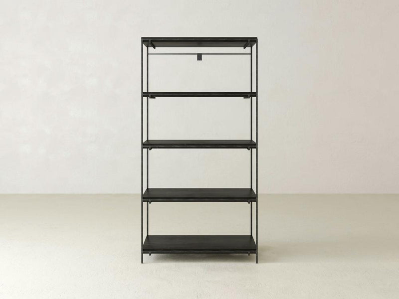 A minimalist Gwen Shelf unit from James+James, featuring five evenly spaced black metal shelves, stands against a plain white wall. The shelves are empty, and the floor is bare, emphasizing the simplicity and clean lines of this industrial design.