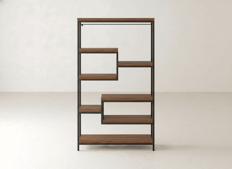The James+James Arlo Shelf is a modern bookshelf with a geometric, zigzag design. It features multiple solid hardwood shelves framed in industrial steel, creating open spaces of varying heights and widths that are perfect for books or decor. The background consists of plain, light-colored walls and floors.
