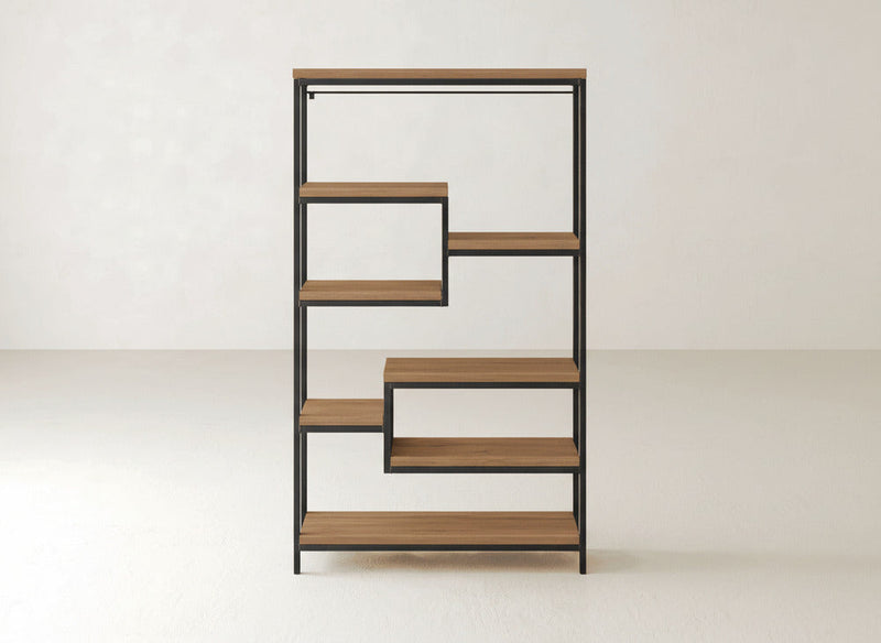 The James+James Arlo Shelf is a modern bookshelf with a geometric, zigzag design. It features multiple solid hardwood shelves framed in industrial steel, creating open spaces of varying heights and widths that are perfect for books or decor. The background consists of plain, light-colored walls and floors.