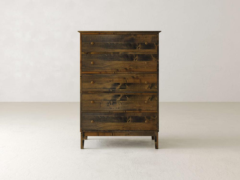 The James & James Bennett Tall Chest, crafted from solid maple wood, stands against a plain, light-colored wall. This elegant dresser features spacious drawers with round wooden knobs and offers ample storage in its simple, traditional design.