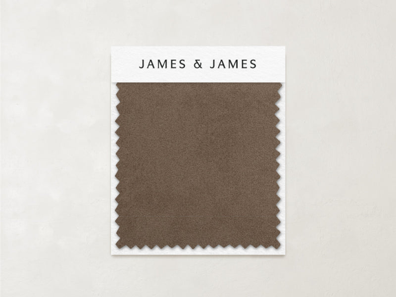 A rectangular caramel-toned "Latte - Velvet Swatch" from James+James, with zigzag edges, rests on a branded card against a light textured background, showcasing its soft texture.