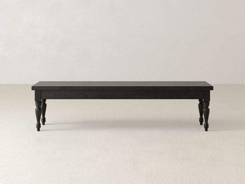Against a plain white background stands the Chateau Bench by James & James, a long dark wooden piece with carved legs. This handcrafted bench offers a simple, classic design and four decorative legs, perfect for adding elegant dining seating that blends style and function.