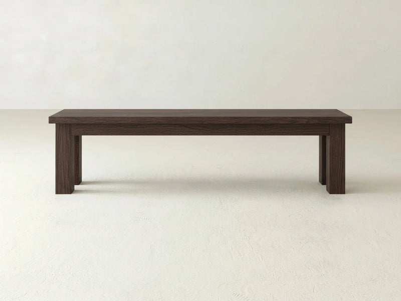 The James+James Farmhouse Bench - Sable on Oak features a simple rectangular design with a dark brown finish, placed on a light-colored floor against a plain, light-colored wall.