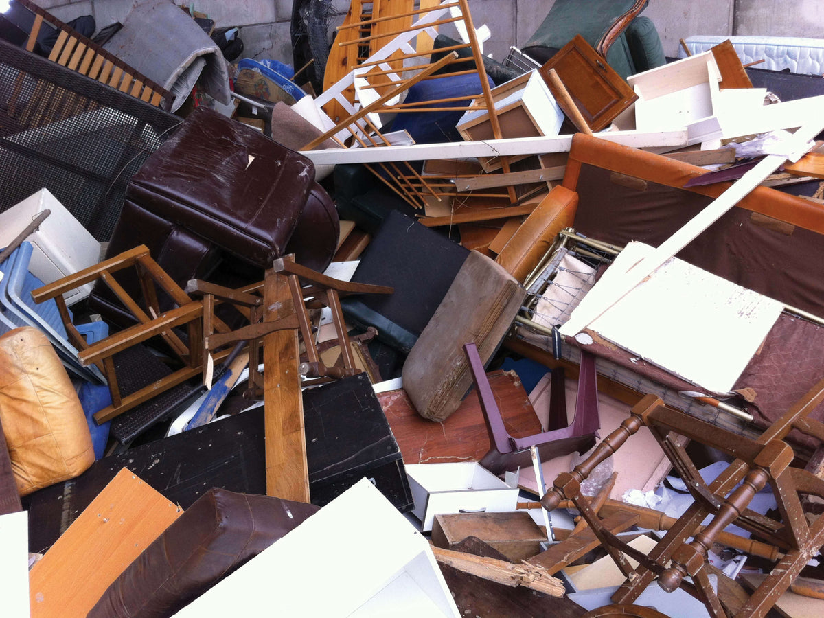 A pile of discarded furniture and debris, including chairs, tables, shelves, and cushions, in a chaotic arrangement. Various materials such as wood, metal, and fabric are visible, with a mix of colors and textures.