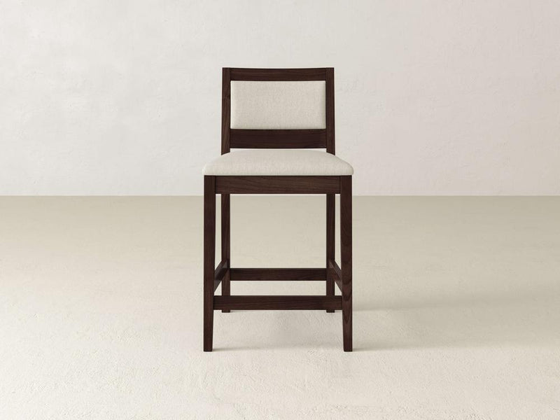 The Gina Side Stool from James & James showcases a modern design with a dark maple wood frame and a light beige fabric seat and backrest, set elegantly against an off-white wall and floor backdrop.