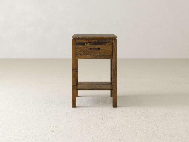 The Jensen 1 Drawer Nightstand by James & James, crafted from solid maple hardwood, showcases a rustic finish with modern simplicity. It features one drawer and an open shelf beneath it, all set against a plain light-colored background in its minimalist design.