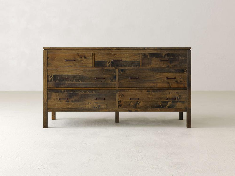 The James & James Jensen 7 Drawer Dresser, made from solid maple hardwood with a rustic finish and dark handles, stands out against light walls and floors. Its natural wood grain enhances any room with a contemporary appearance.