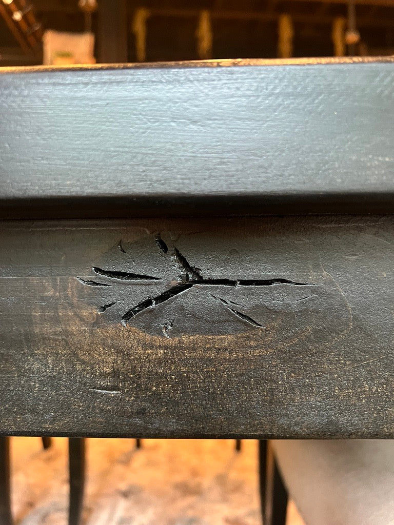 Close-up of a dark wooden surface with a visible crack, exposing splintered fibers. The background is blurred, hinting at a room setting.