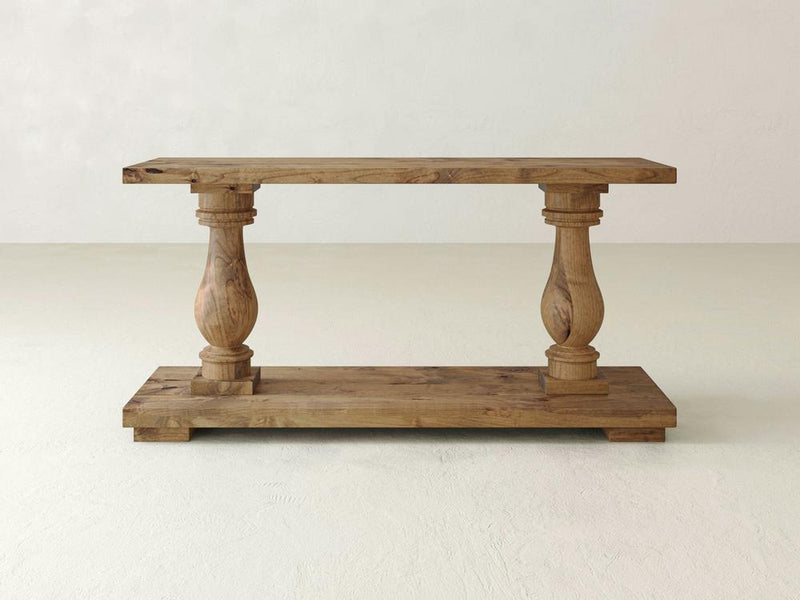 The James+James Vivien Sofa Table in Harvest Wheat features a rectangular top and bottom shelf, supported by two ornately carved, wide cylindrical legs. Its natural wood finish with visible grain patterns beautifully combines traditional and rustic elements.