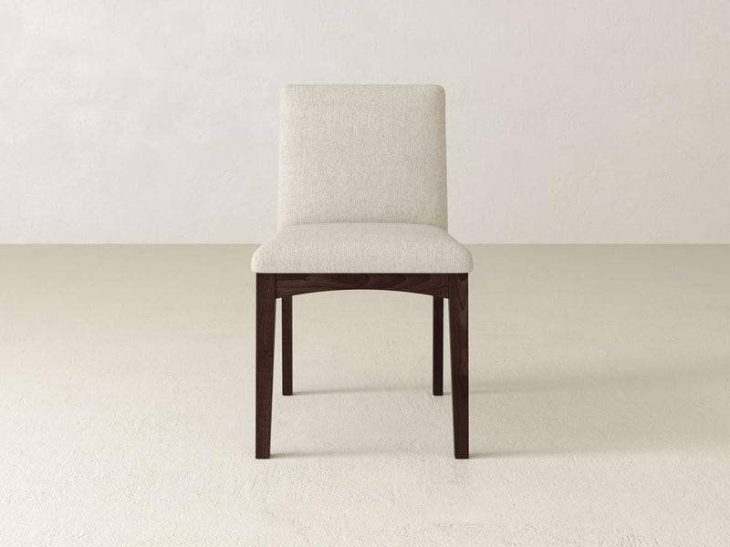 The Klein Dining Chair by James & James features a cream upholstered seat and backrest, elegantly supported by maple wooden legs against a plain, light-colored wall and floor.