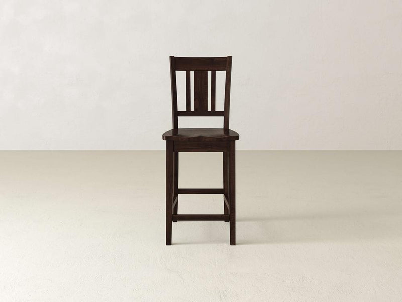 The William Stool by James & James exudes timeless sophistication on a plain light floor against an off-white wall. This elegant dark wooden piece features a slatted backrest and footrest, blending seamlessly into any home decor with its simple yet refined design.