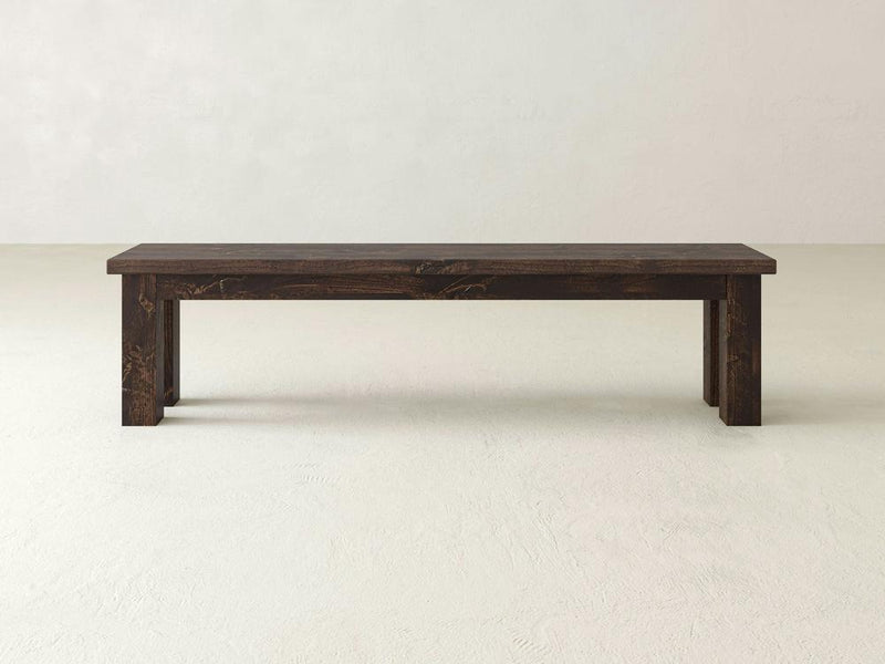 The James+James Farmhouse Bench - Tobacco on Alder features a simple rectangular design with a dark brown finish, four sturdy legs, and a flat seat without backrest or armrests, set against a light background.