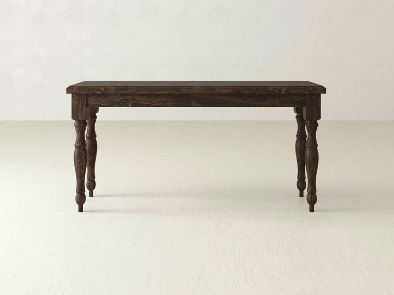 The Abigail Sofa Table by James+James, featuring a dark wooden rectangular top and ornate, carved legs, stands on a light-colored floor against a plain, light-colored wall. The table boasts a rustic appearance with its traditional design in a rich Tobacco finish.