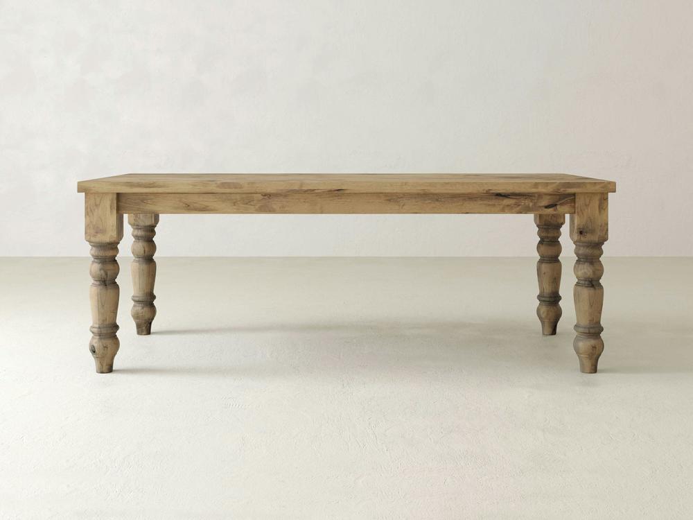 The Baluster Dining Table - Harvest Wheat by James+James is centered against a plain, light-colored background. The rectangular wooden table, with a natural finish, features four turned legs and a simple, rustic design.