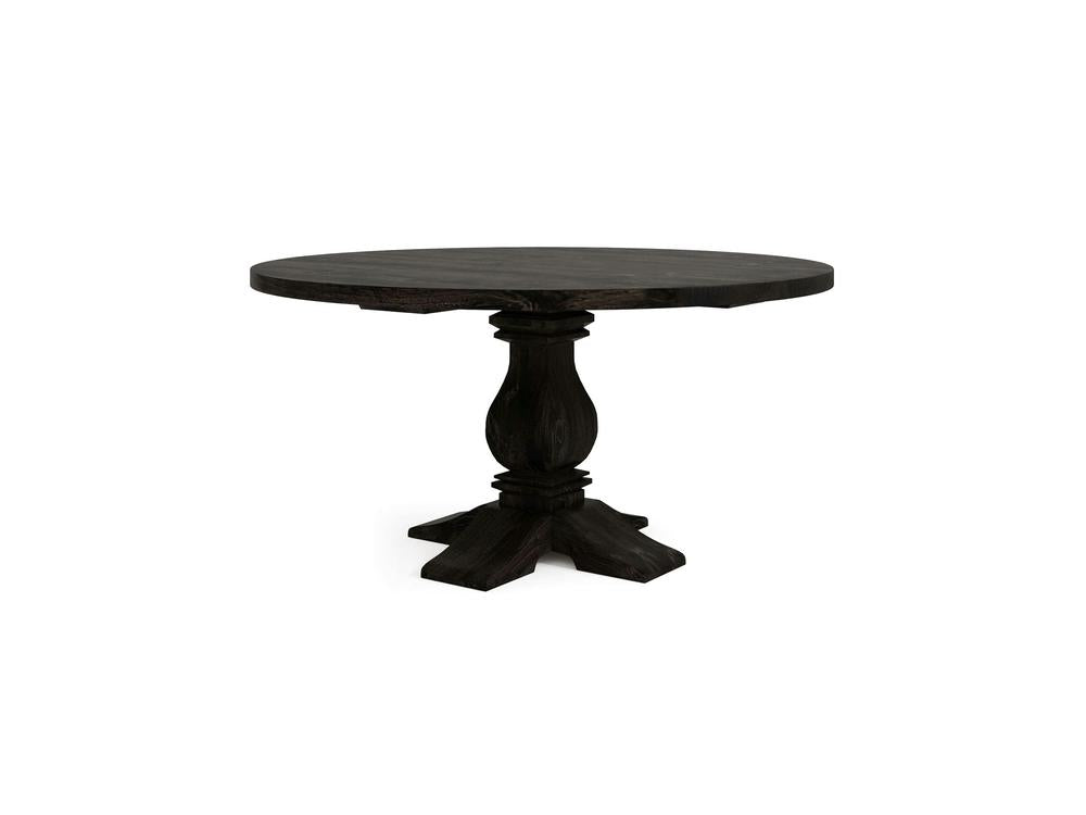 The Heirloom Round Dining Table - Charred Ember by James+James features a dark wooden round tabletop with a slight sheen, supported by a thick pedestal base adorned with intricate carvings. The four sturdy legs extend outward for balanced support against a plain white background.