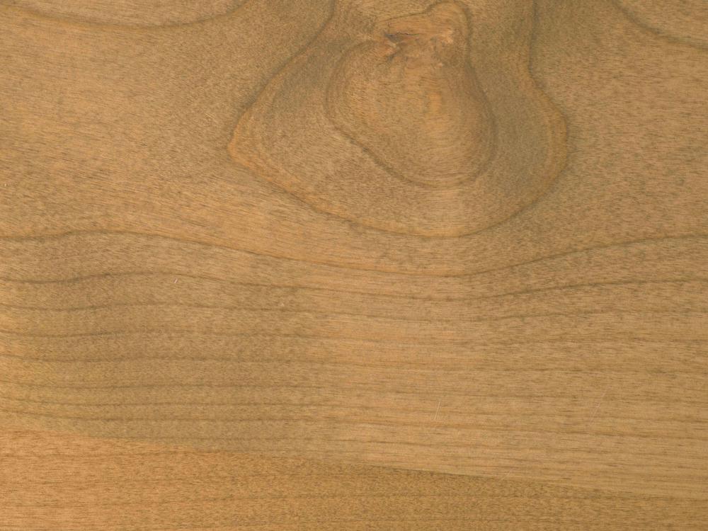 A close-up of the Olivia Bench by James+James in Harvest Wheat on Alder, highlighting its light brown wood surface with natural grain patterns and a prominent knot near the top center.