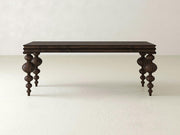 The Olivia Sofa Table - Tobacco by James+James, featuring a dark wooden finish and four intricately carved, spindle-style legs, stands against a plain, light-colored background. The table boasts a rectangular top with a simple, flat surface.