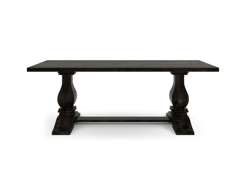 The Heirloom Dining Table - Charred Ember by James+James features a dark wooden rectangular top and two intricately carved pedestal legs connected by a horizontal stretcher base. Its traditional and elegant design makes it suitable for a formal dining room setting.