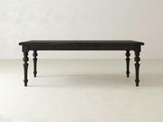 The Allyson Dining Table - Charred Ember by James+James, featuring intricately carved legs, stands against a plain, light-colored background. The table has a rectangular shape with a smooth, polished surface that highlights its minimalist yet elegant design.