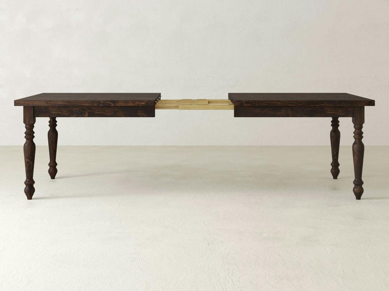 The James+James French Country Expandable Dining Table - Tobacco features a dark wooden finish and turned legs, displayed in an extended position with a leaf section visible in the middle. The neutral background highlights the table's rich finish and timeless design.