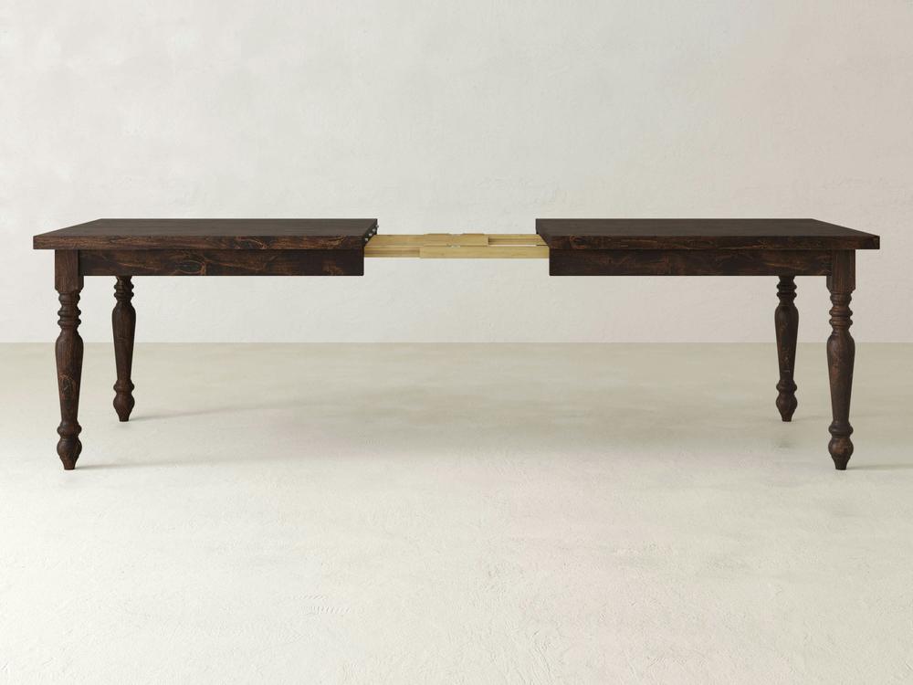 The James+James French Country Expandable Dining Table - Tobacco features a dark wooden finish and turned legs, displayed in an extended position with a leaf section visible in the middle. The neutral background highlights the table's rich finish and timeless design.