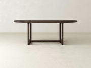 An Emersen Oval Dining Table - Tobacco by James+James with a wooden top and sturdy, rectangular legs is placed in a minimalist room with neutral-colored walls and floors.