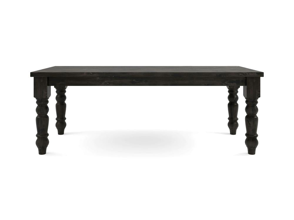 The Baluster Dining Table - Charred Ember by James+James features a dark wooden rectangular top supported by four intricately carved legs. Its simple yet elegant design makes it versatile for various interior styles while the visible wood grain enhances its rustic aesthetic.