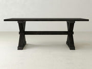 The Trestle Dining Table - Charred Ember by James+James features a dark wooden surface with a rectangular top set on trestle-style legs. This table showcases a clean, minimalist design and is placed against a plain, light-colored background.