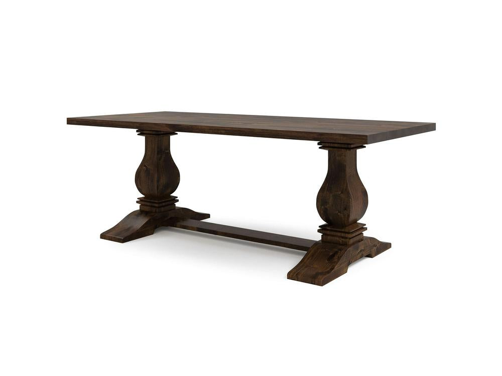 The Heirloom Dining Table - Tobacco by James+James features a dark wooden rectangular top supported by two ornate, pedestal-style legs connected by a horizontal beam at the base. This table exudes a classic, rustic design and boasts an elegant, sturdy appearance.