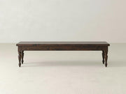 The James & James Chateau Bench - Tobacco features a simple, rustic design with dark wood and four turned legs, set against a plain, light-colored background.