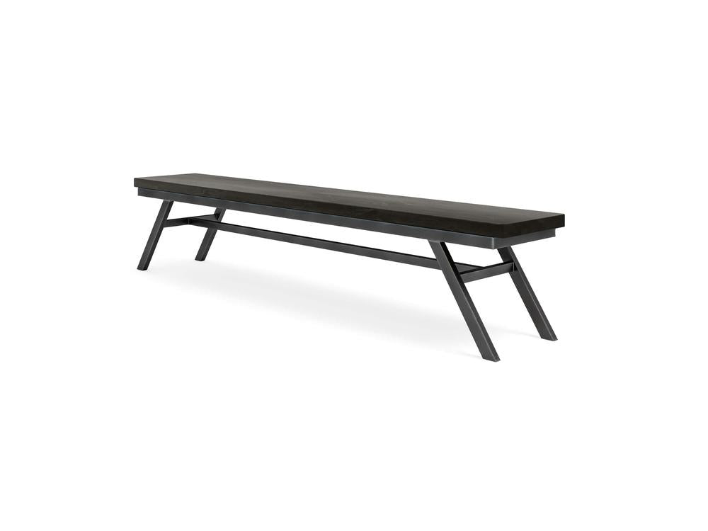 The James+James Fulton Bench in Charred Ember on Alder features a modern, minimalist design with a rectangular seat and slanted legs joined by a horizontal bar, displayed against a plain white background.