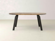 The Fulton Oval Dining Table by James+James features a modern industrial design with an oval, solid hardwood top and a smooth light brown surface. It is supported by four angled raw steel legs, creating a minimalist and contemporary look, all set against a neutral, light-colored background.