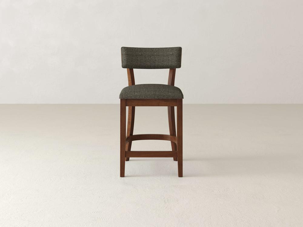 The James & James Everly Upholstered Stool, with its mid-century wooden design, showcases a dark green seat and backrest. It complements any plain, light-colored floor against a neutral backdrop, exuding simple modern elegance.
