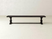 The James+James Heirloom Bench in Charred Ember on Alder features a rectangular seat and carved legs, set on a light floor against an off-white wall.