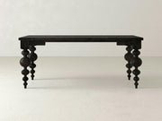 In a minimalist, light-colored room, an Olivia Desk - Charred Ember by James+James stands alone. This black, rectangular wooden desk boasts a smooth top and four intricately carved baluster-style legs that add a touch of elegance to its simple design.