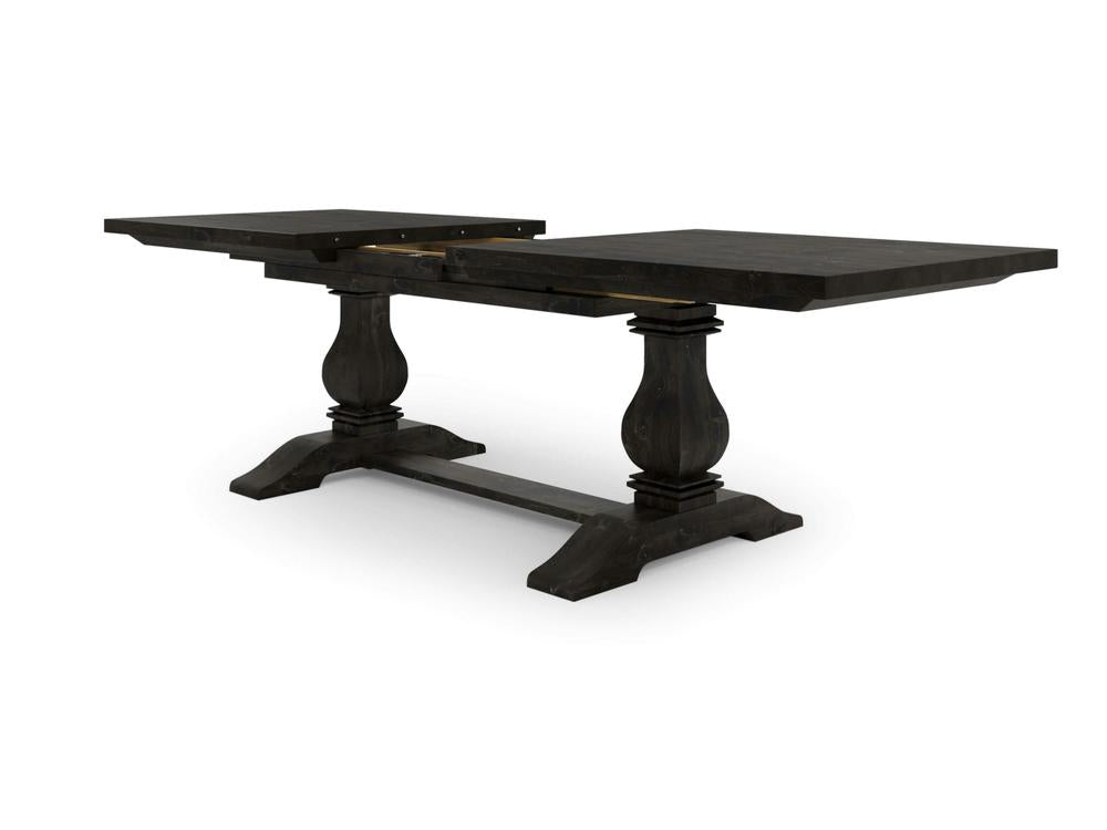 The Heirloom Expandable Dining Table - Charred Ember by James+James is depicted with its elegant double pedestal legs in view. The table is shown partially extended, displaying the leaf sections that are visible but not fully assembled. The sturdy base includes a crossbar for additional support.