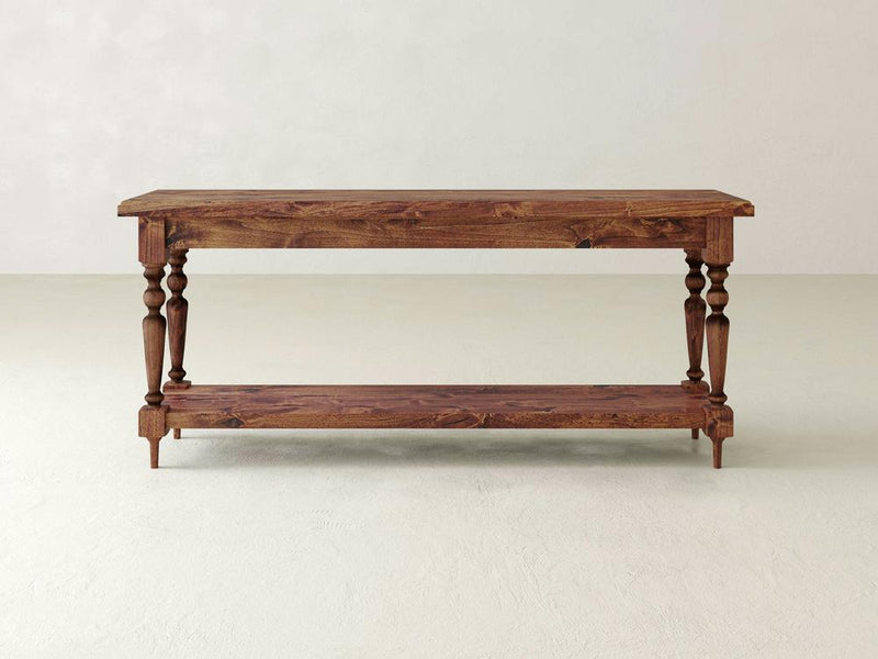 The Ella Sofa Table - Tuscany by James+James is a wooden console table featuring an upper and lower surface with four intricately carved legs. Boasting a natural wood finish, the table stands on a smooth, light-colored floor against a light background.