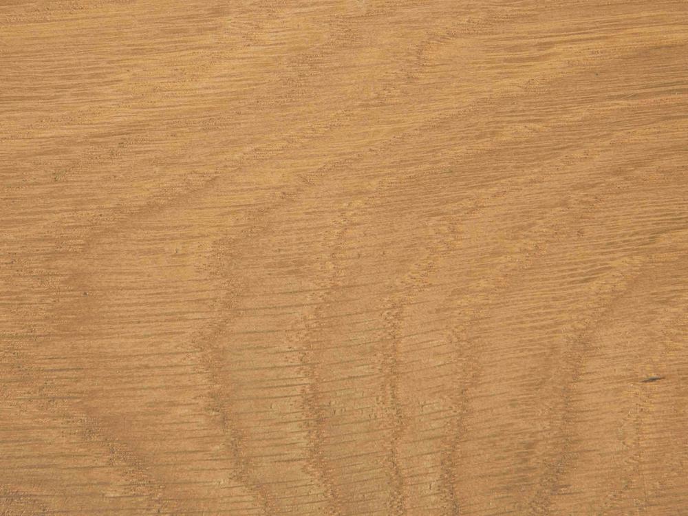 A close-up view of the Francesca Dining Table - Satin by James+James reveals its finely crafted surface with elegant, subtle grain lines, reminiscent of a textured desert landscape. The wood tones range from light tan to darker brown, showcasing natural variations in the material. No other objects are present.