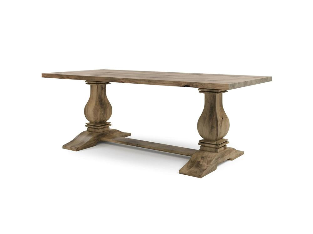 The Heirloom Dining Table - Harvest Wheat by James+James is a wooden rectangular dining table with a polished surface. It features sturdy, carved double pedestal legs that connect to a horizontal support beam at their bases. The table has a natural wood grain finish and is placed against a plain white background.