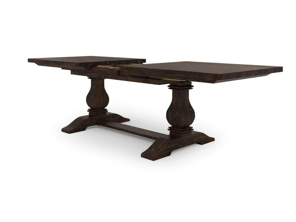 The Heirloom Expandable Dining Table - Tobacco by James+James is a dark wooden table with a rectangular top and a trestle base, featuring two ornate pedestal legs. The tabletop is divided and extended, showcasing its expandable design. It has a distressed finish, giving the table a rustic appearance.