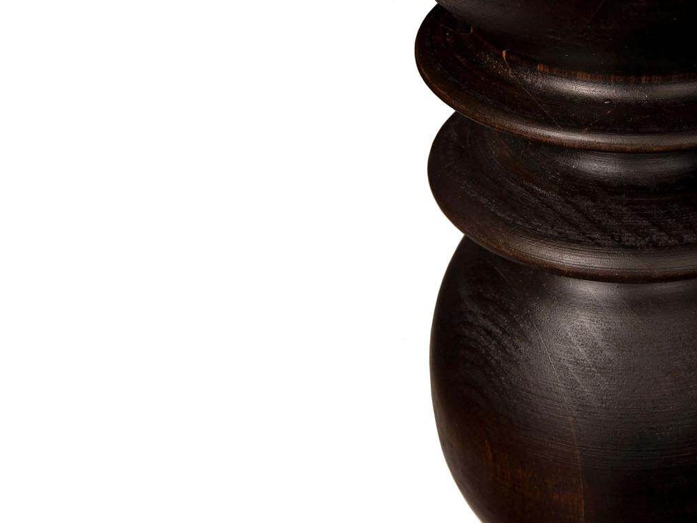 Close-up of a leg from the Bailey Dining Table - Tobacco by James+James, showcasing its polished and smooth dark wooden surface with a rounded, ornate design. The rich, dark finish and visible grain stand out against the plain, bright white background, highlighting the intricate detailing and texture of the wood.