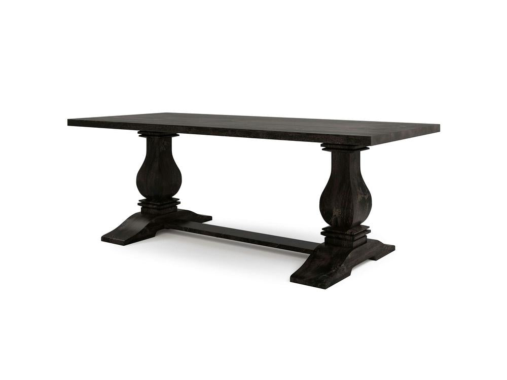 The Heirloom Dining Table - Charred Ember by James+James boasts a rectangular wooden top with a dark finish. It features two ornate pedestal legs connected by a horizontal support beam at the base and showcases classic carved details on the legs, lending it a traditional look.