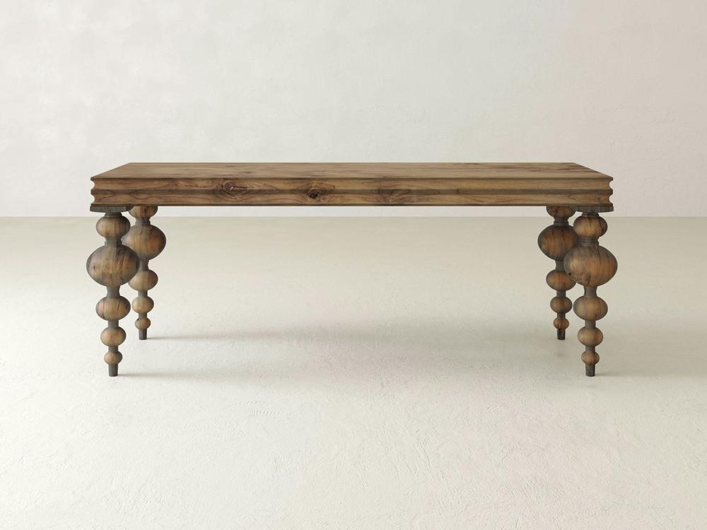 The Olivia Sofa Table - Harvest Wheat by James+James is a wooden table with a rectangular top showcasing a natural wood grain finish. It's supported by four uniquely designed legs, each carved into a combination of spherical and cylindrical shapes, creating an artistic and elegant look against a plain, off-white background.