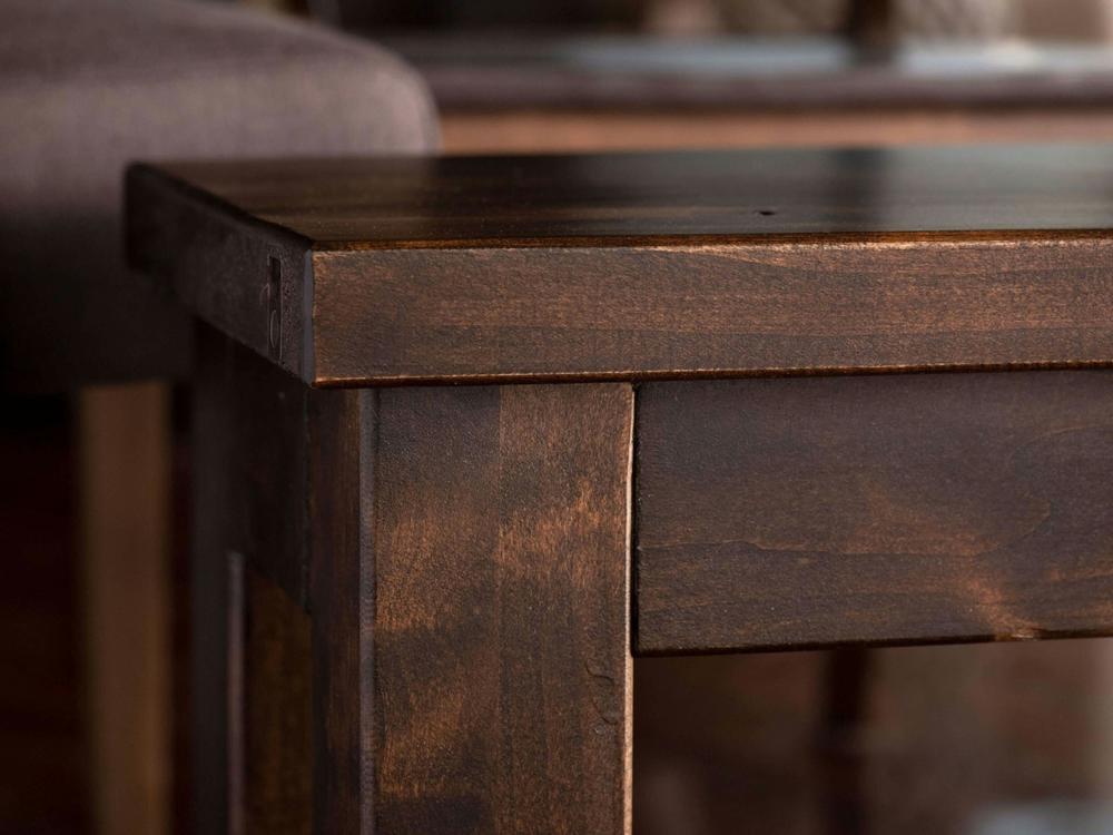 Close-up of the corner of the James+James Farmhouse Bench - Tobacco on Alder, highlighting its smooth finish, wood grain, and joinery. A portion of a cushioned seat appears in the background.
